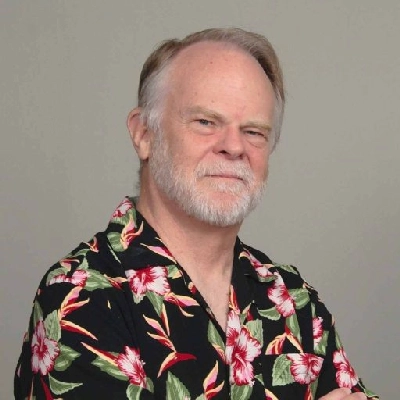This image portrays Byron Harvey wearing a floral-patterned shirt with arms crossed.