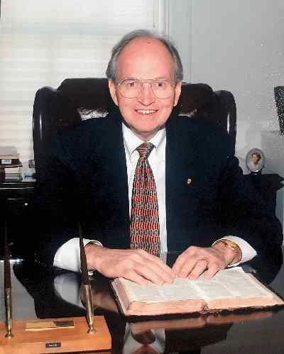 Pastor Robert L. Alderman seated at a desk with an open Bible and pens.